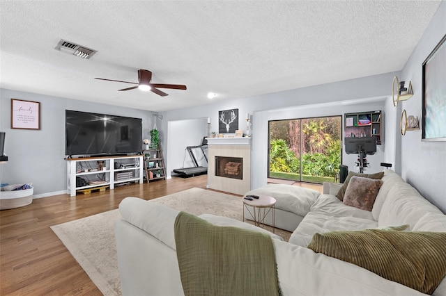 living room featuring a textured ceiling, a fireplace, wood finished floors, visible vents, and baseboards