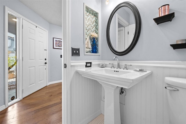 bathroom with toilet, wainscoting, a sink, a textured ceiling, and wood finished floors