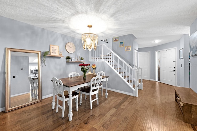 dining space featuring stairs, a textured ceiling, wood finished floors, and an inviting chandelier