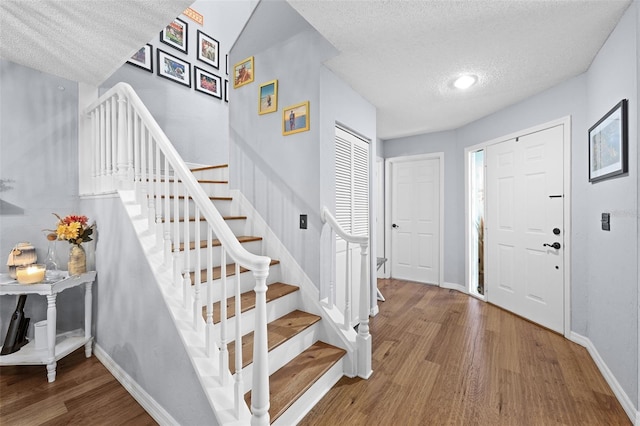 foyer entrance with stairs, a textured ceiling, baseboards, and wood finished floors