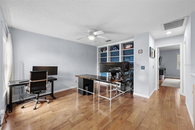 office area featuring a textured ceiling, wood finished floors, visible vents, baseboards, and a ceiling fan