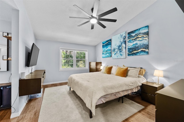 bedroom featuring baseboards, ceiling fan, wood finished floors, vaulted ceiling, and a textured ceiling