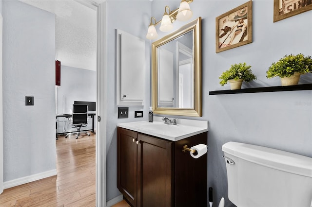 bathroom featuring toilet, a textured ceiling, vanity, wood finished floors, and baseboards