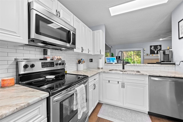 kitchen featuring stainless steel appliances, white cabinetry, a sink, and wood finished floors