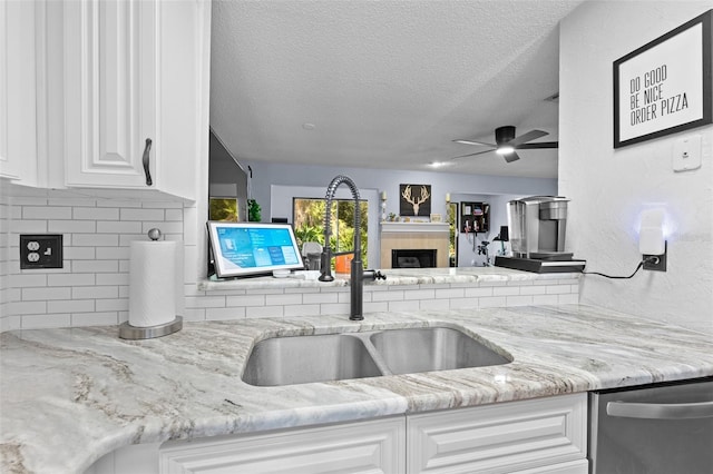 kitchen featuring decorative backsplash, a sink, light stone countertops, a fireplace, and stainless steel dishwasher