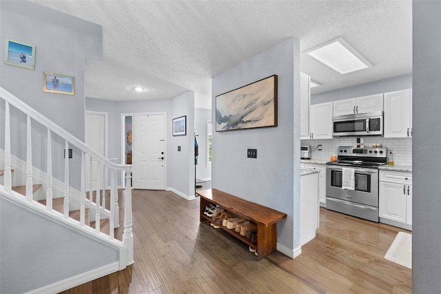 kitchen with appliances with stainless steel finishes, white cabinets, light wood-style flooring, and tasteful backsplash