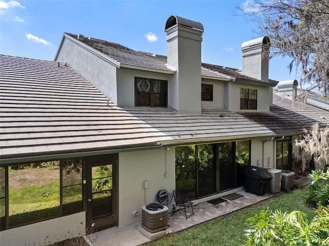 rear view of property featuring a chimney, a patio area, central AC, and stucco siding