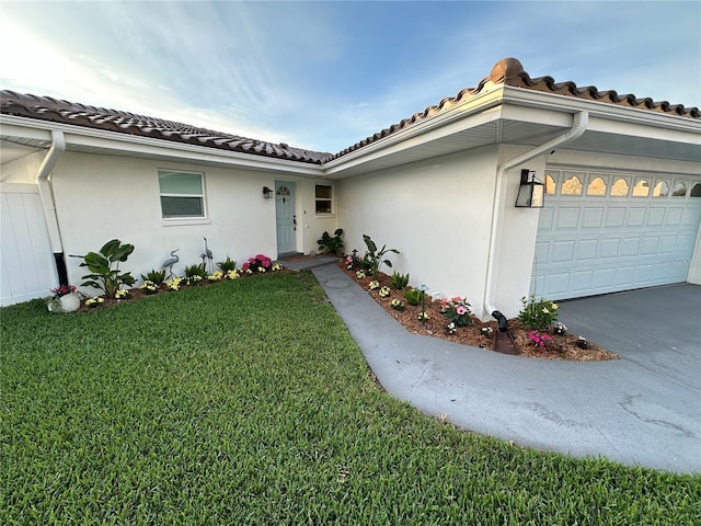 exterior space with an attached garage, a tiled roof, a lawn, and stucco siding