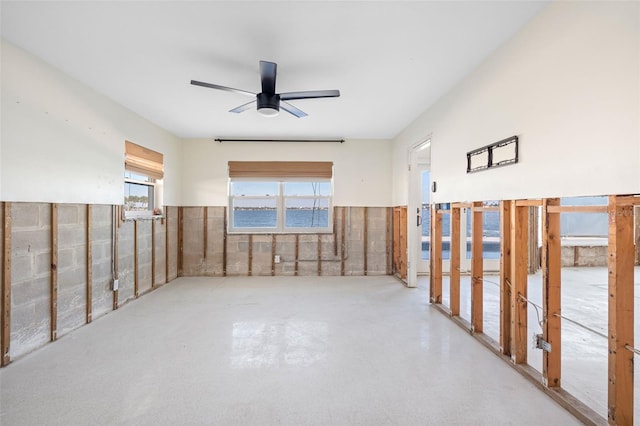 empty room featuring a water view, ceiling fan, and wainscoting