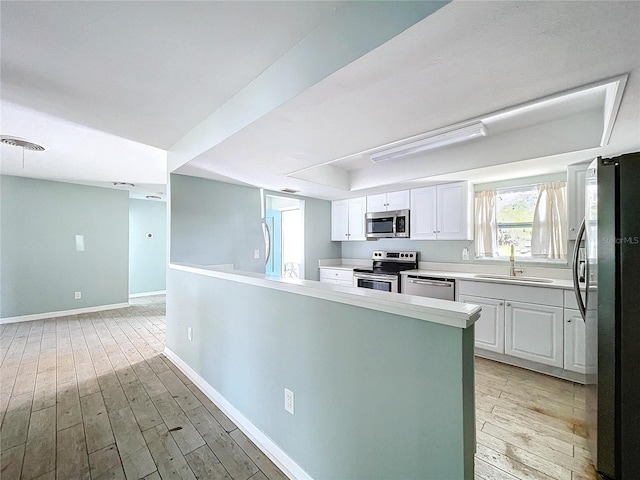 kitchen featuring white cabinets, appliances with stainless steel finishes, a peninsula, light countertops, and a sink