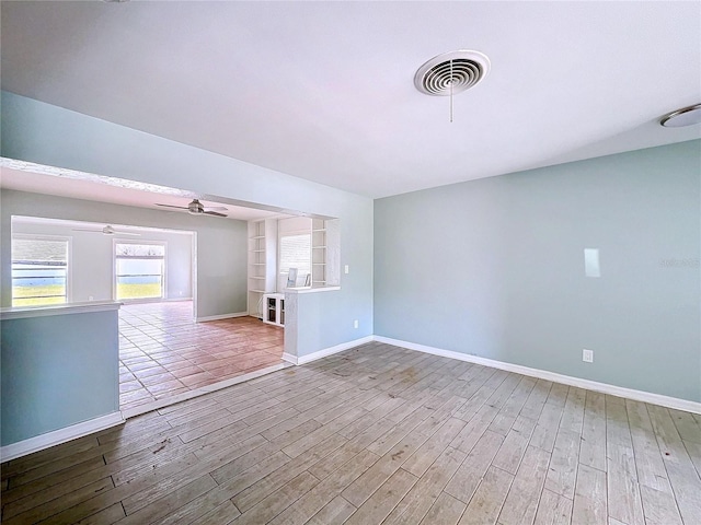 spare room with light wood-style floors, ceiling fan, visible vents, and baseboards