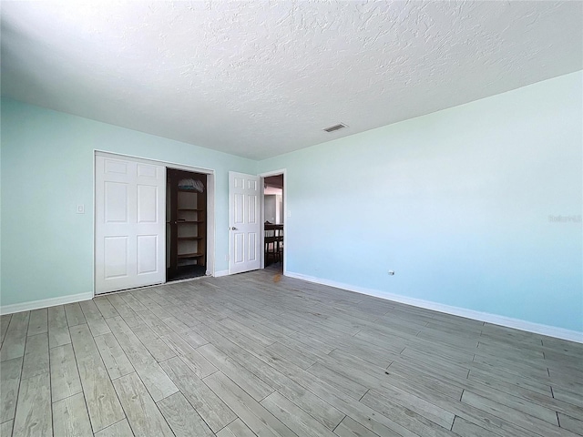 unfurnished bedroom featuring visible vents, a textured ceiling, baseboards, and wood finished floors