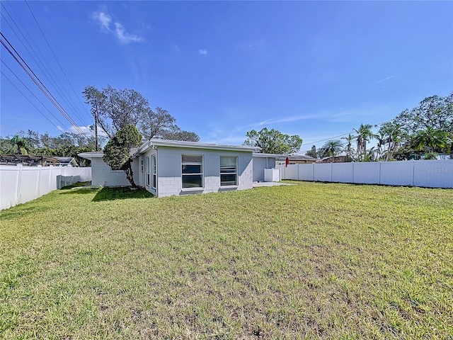 rear view of house featuring a lawn, concrete block siding, and a fenced backyard