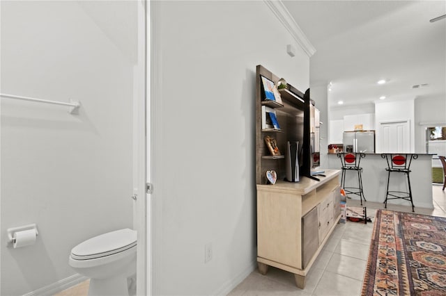 kitchen with light tile patterned floors, stainless steel fridge with ice dispenser, ornamental molding, light brown cabinets, and a kitchen bar