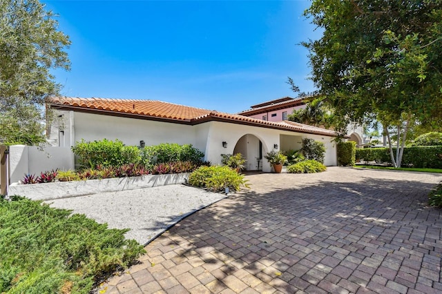 mediterranean / spanish home featuring a tiled roof, an attached garage, fence, decorative driveway, and stucco siding