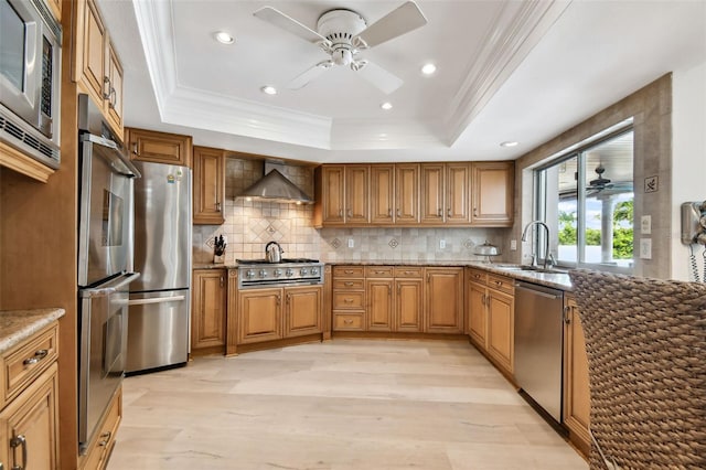 kitchen with stone countertops, stainless steel appliances, brown cabinets, wall chimney exhaust hood, and a tray ceiling