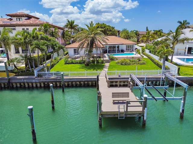 dock area featuring boat lift, a water view, a lawn, a fenced backyard, and an outdoor pool