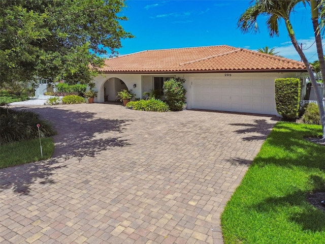 mediterranean / spanish-style house with an attached garage, a tile roof, decorative driveway, and stucco siding