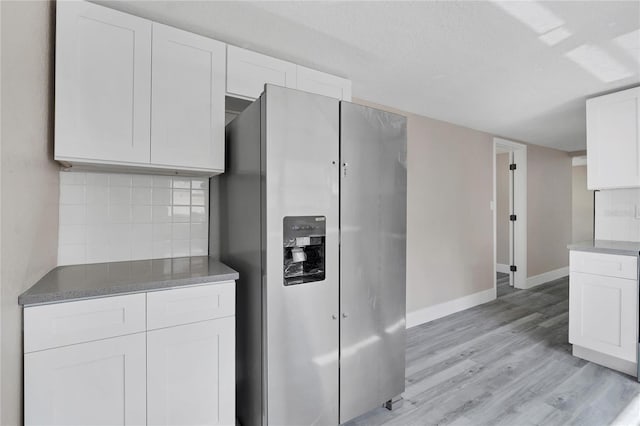 kitchen featuring white cabinetry, tasteful backsplash, a textured ceiling, light wood-type flooring, and stainless steel fridge