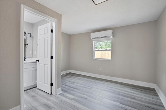 empty room featuring light hardwood / wood-style floors, a wall unit AC, and a textured ceiling