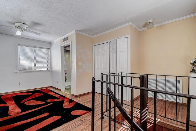 bedroom with a textured ceiling, wood finished floors, visible vents, ornamental molding, and a closet