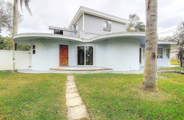 back of property featuring a gate, a lawn, fence, and stucco siding