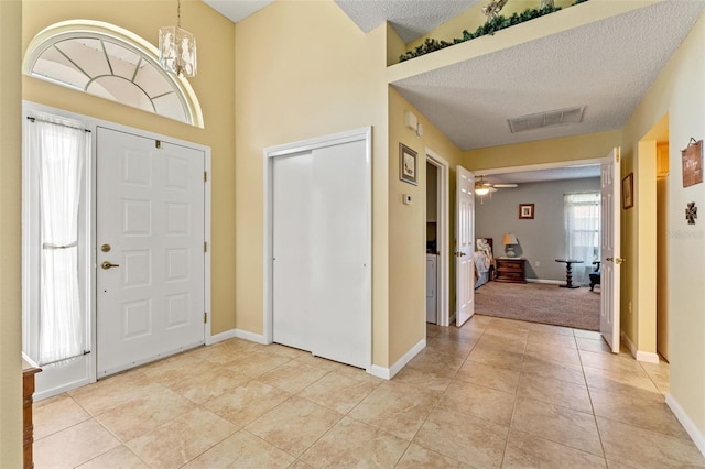 foyer entrance featuring ceiling fan with notable chandelier, light tile patterned floors, and a textured ceiling