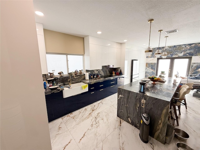 kitchen featuring hanging light fixtures, a spacious island, sink, tasteful backsplash, and white cabinets