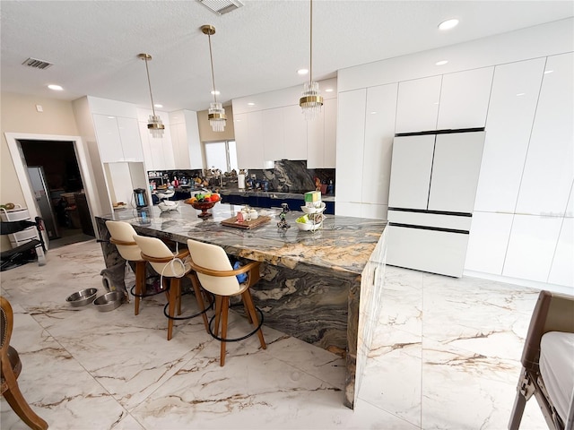 kitchen featuring white fridge, white cabinetry, a textured ceiling, and decorative light fixtures