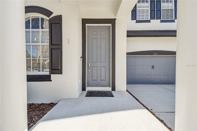 view of exterior entry with a garage, driveway, and stucco siding