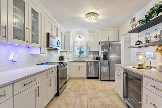 kitchen with sink, appliances with stainless steel finishes, white cabinetry, light stone counters, and beverage cooler