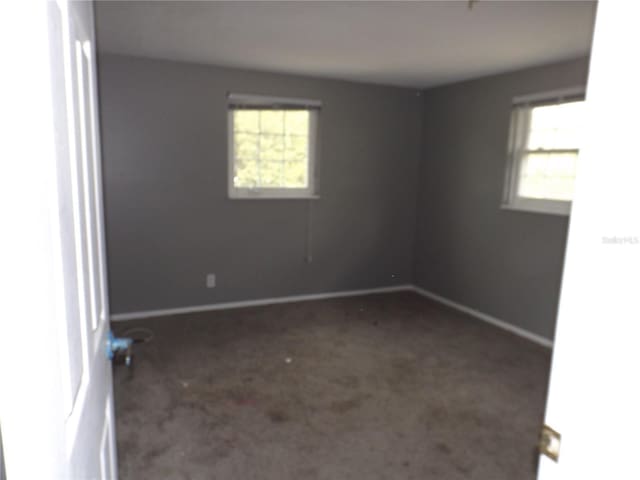 spare room with dark colored carpet, a healthy amount of sunlight, and baseboards