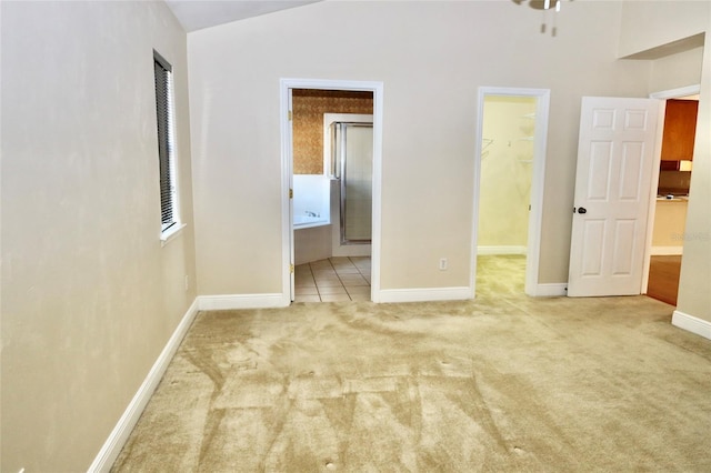 unfurnished bedroom with light carpet, vaulted ceiling, and ensuite bath