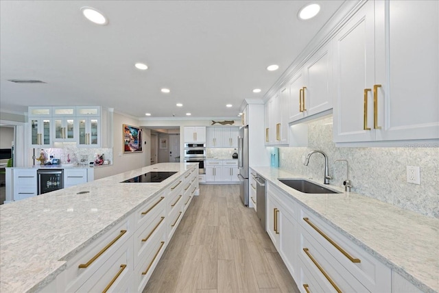 kitchen with light wood finished floors, appliances with stainless steel finishes, white cabinets, a sink, and beverage cooler