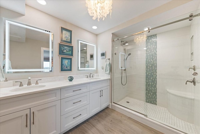 full bath with a stall shower, an inviting chandelier, a sink, and wood finished floors