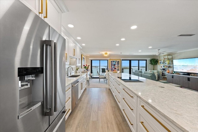 kitchen with light wood finished floors, appliances with stainless steel finishes, crown molding, white cabinetry, and a sink