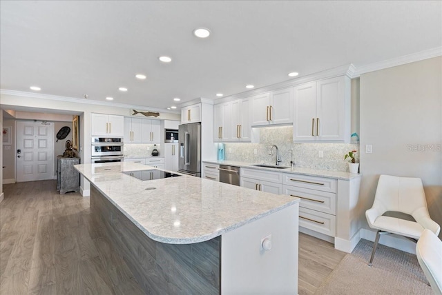 kitchen featuring ornamental molding, stainless steel appliances, a large island with sink, white cabinetry, and a sink