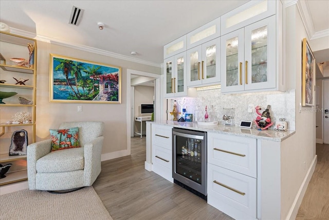 bar with crown molding, tasteful backsplash, a bar, light wood-type flooring, and beverage cooler