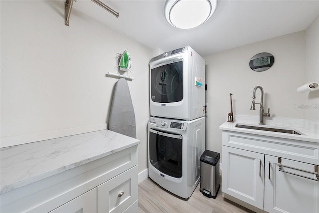 laundry area featuring stacked washer / drying machine, cabinet space, a sink, and light wood-style flooring