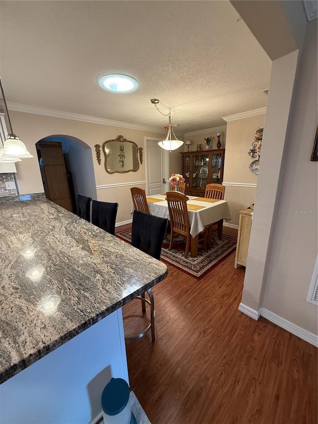dining room featuring baseboards, wood finished floors, arched walkways, and ornamental molding