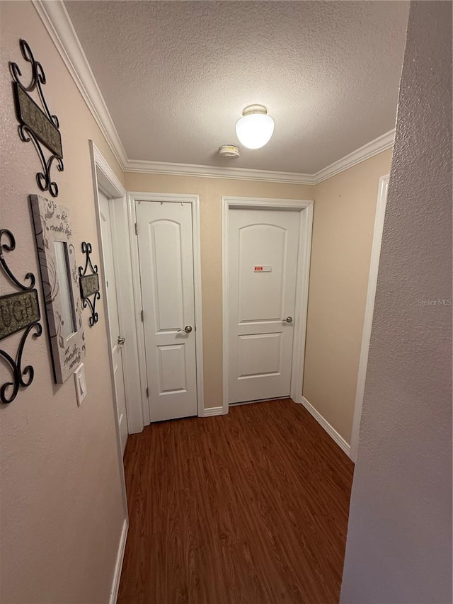 hall with baseboards, a textured ceiling, ornamental molding, and dark wood-style flooring