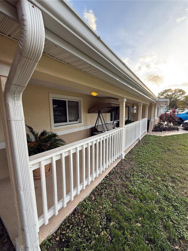 view of side of home featuring a porch, a lawn, and stucco siding