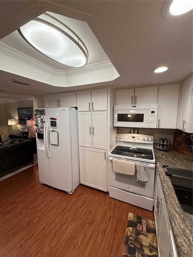 kitchen with a sink, wood finished floors, white appliances, a raised ceiling, and ornamental molding