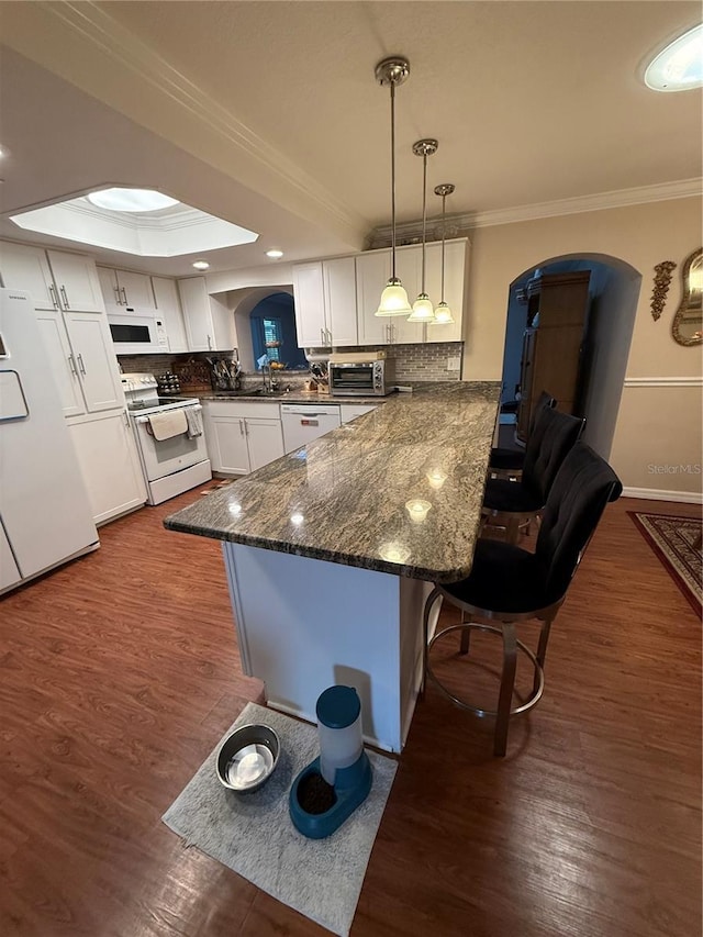 kitchen with a peninsula, a kitchen breakfast bar, arched walkways, white appliances, and ornamental molding