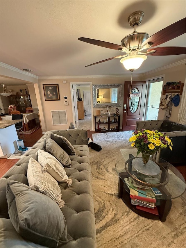 living area featuring visible vents, a ceiling fan, and ornamental molding