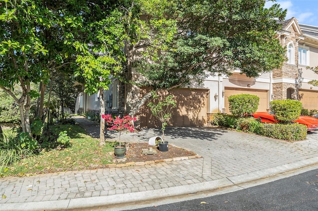 view of property hidden behind natural elements featuring stone siding, decorative driveway, and stucco siding