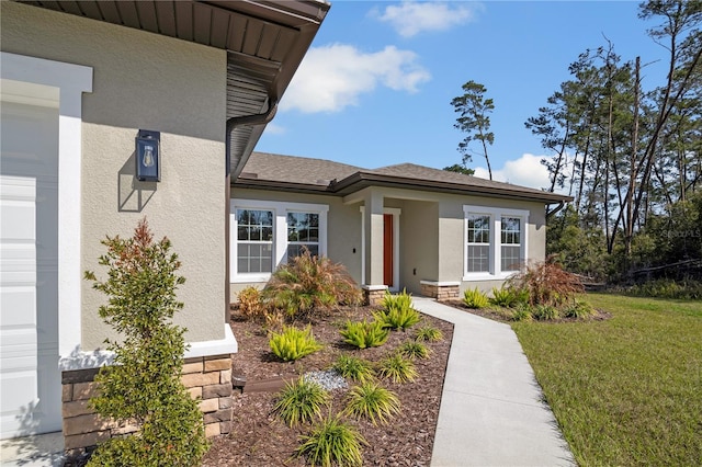 view of exterior entry featuring roof with shingles, a yard, an attached garage, and stucco siding