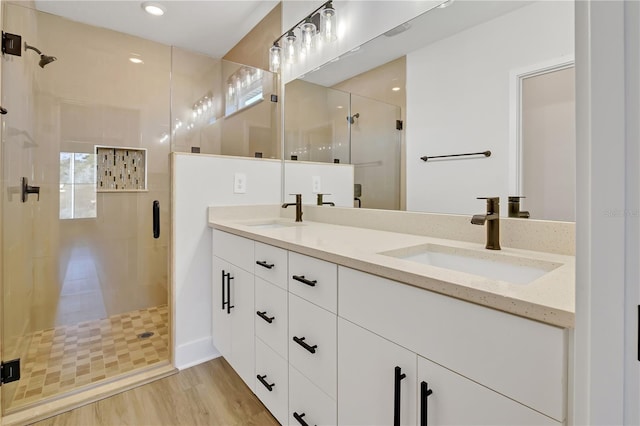 bathroom with double vanity, wood finished floors, a sink, and a shower stall