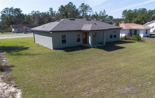 back of house with a yard, roof with shingles, and stucco siding