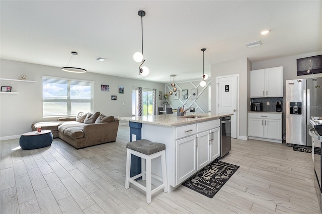 kitchen featuring a kitchen island with sink, stainless steel appliances, white cabinets, open floor plan, and pendant lighting